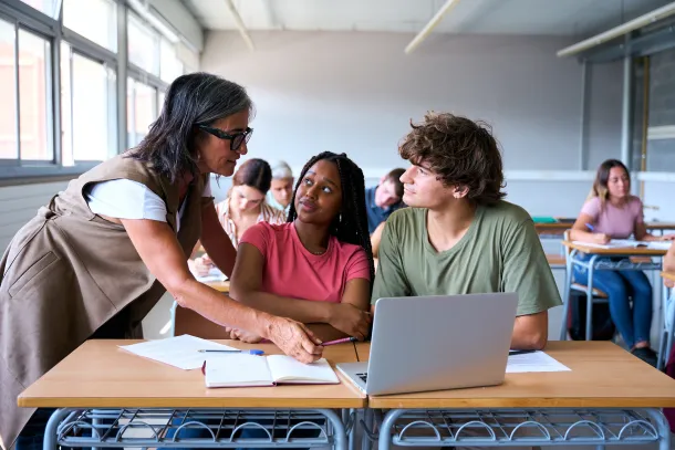 A teacher helping students working together with a laptop in a classroom.